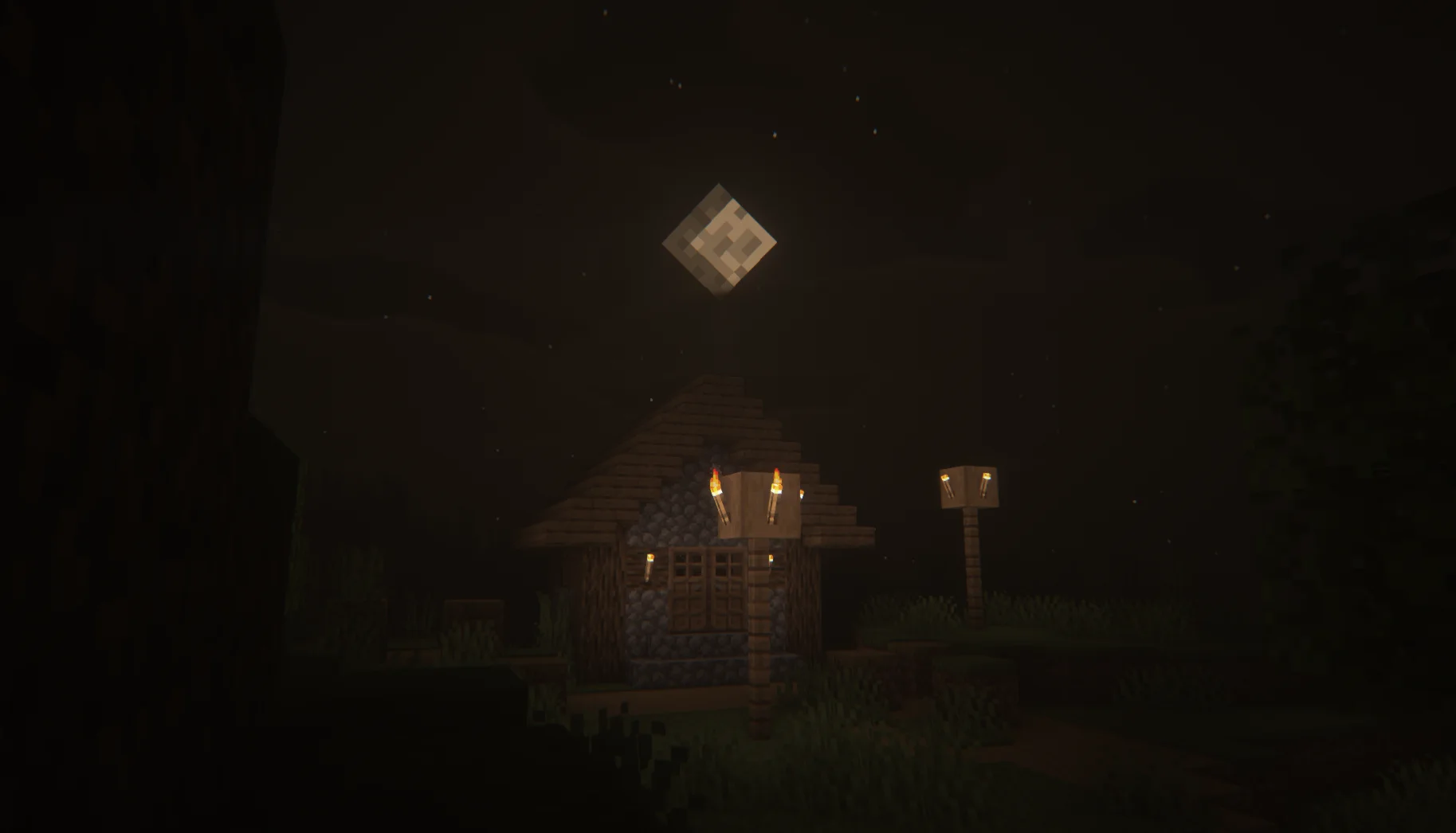 A torch-lit house and lamp posts on a very dark night beneath a full moon.